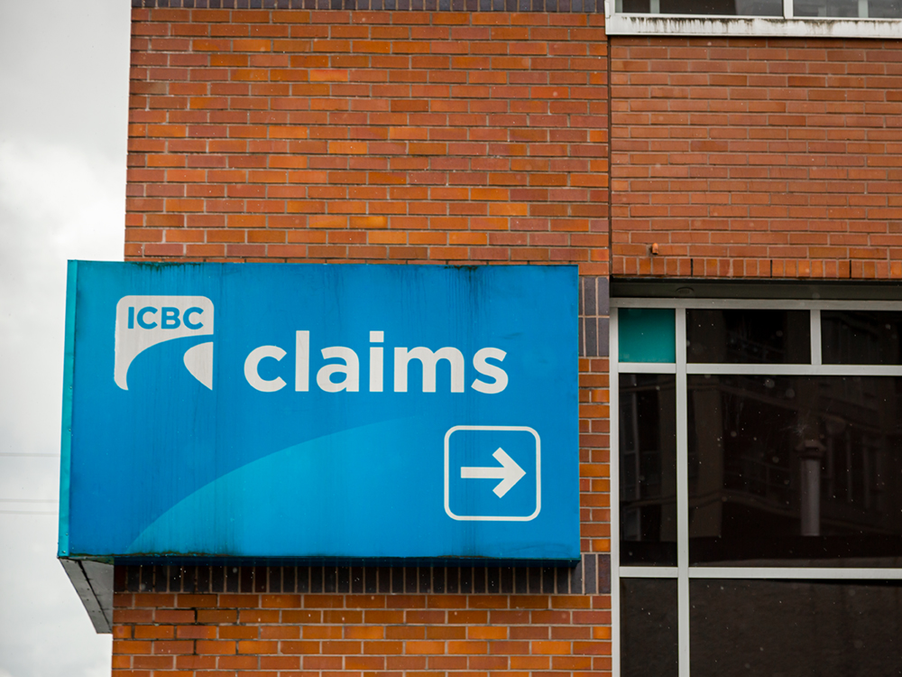 An 'ICBC claims' sign, a bit weather-worn, on the side of a red brick building.