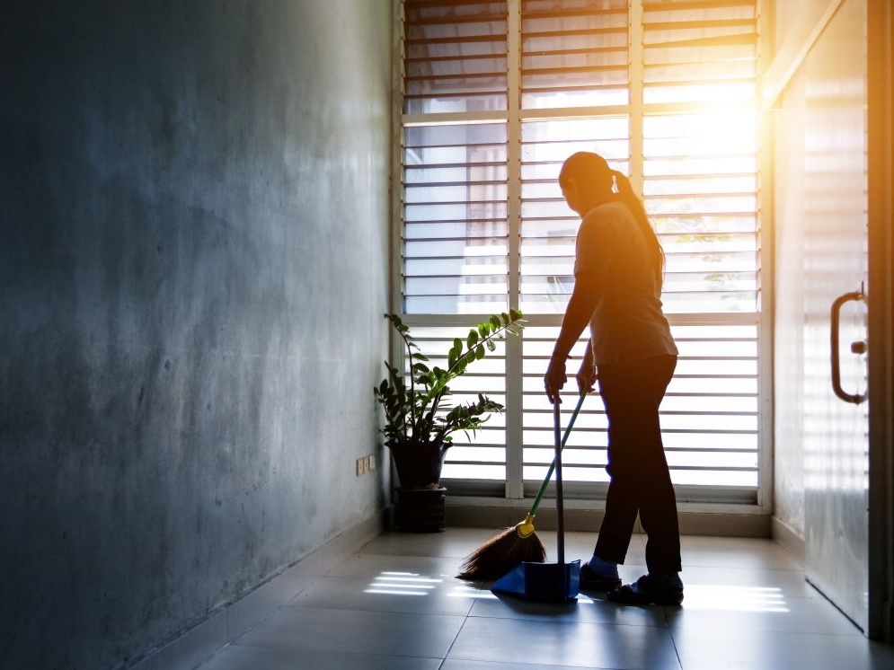 A woman wearing a long ponytail uses a broom and dustpan.