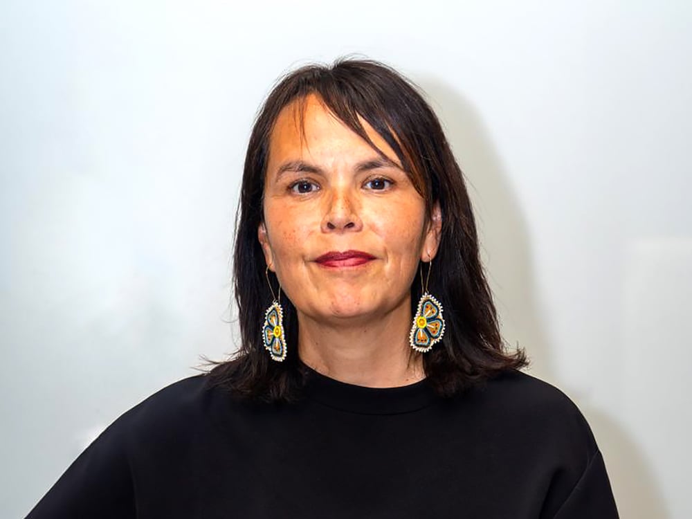 Lorena Sekwan Fontaine, an Indigenous woman with shoulder-length dark hair and medium-light skin tone, looks directly at the camera. She is wearing a black shirt and beaded earrings.