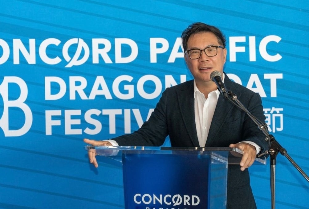 Terry Hui stands at a podium that reads 'Concord Pacific' with the words 'Concord Pacific Dragon Boat Festival' in white lettering on a blue background behind him. He has short black hair and square-framed glasses and is wearing a dark suit jacket over a white button-down shirt.