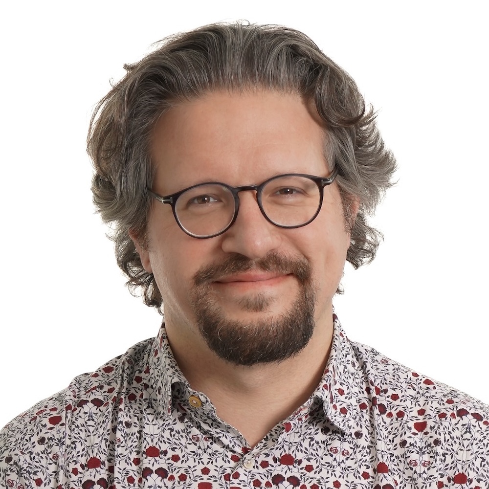 Headshot of a light-skinned man with brown hair and goatee, glasses and a patterned shirt.