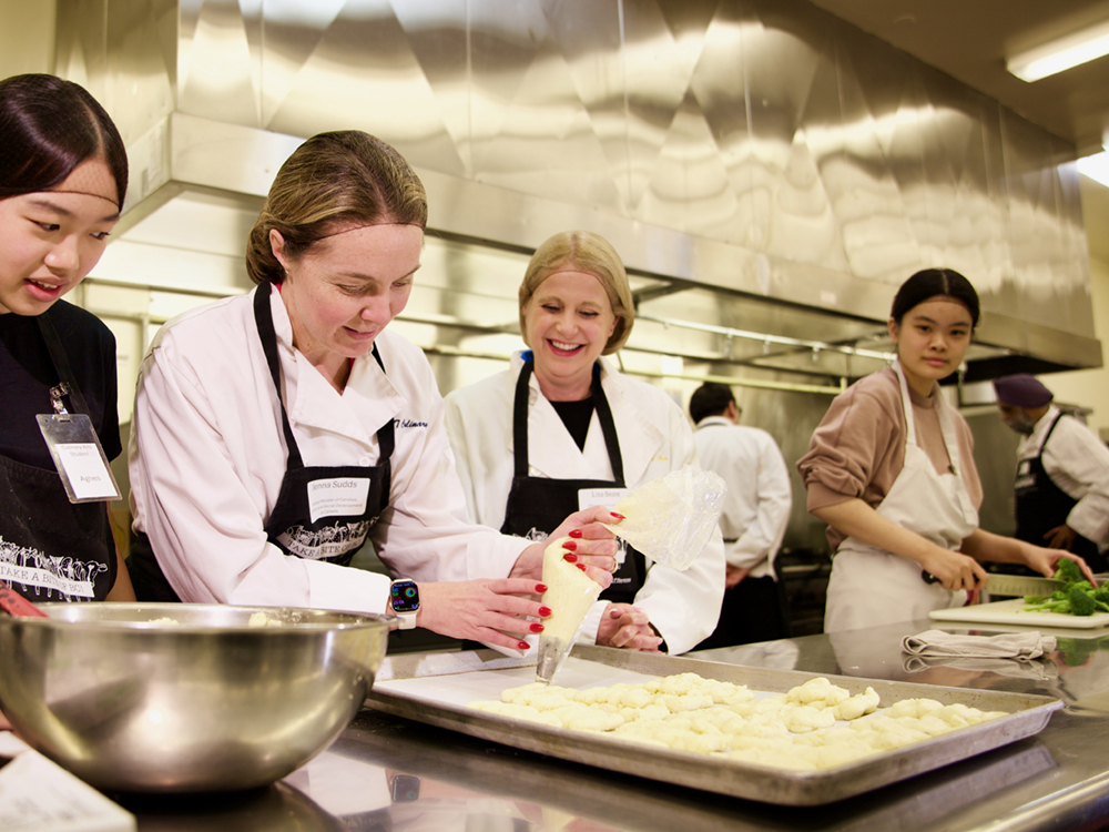 Four people stand at a table preparing piped pastries.