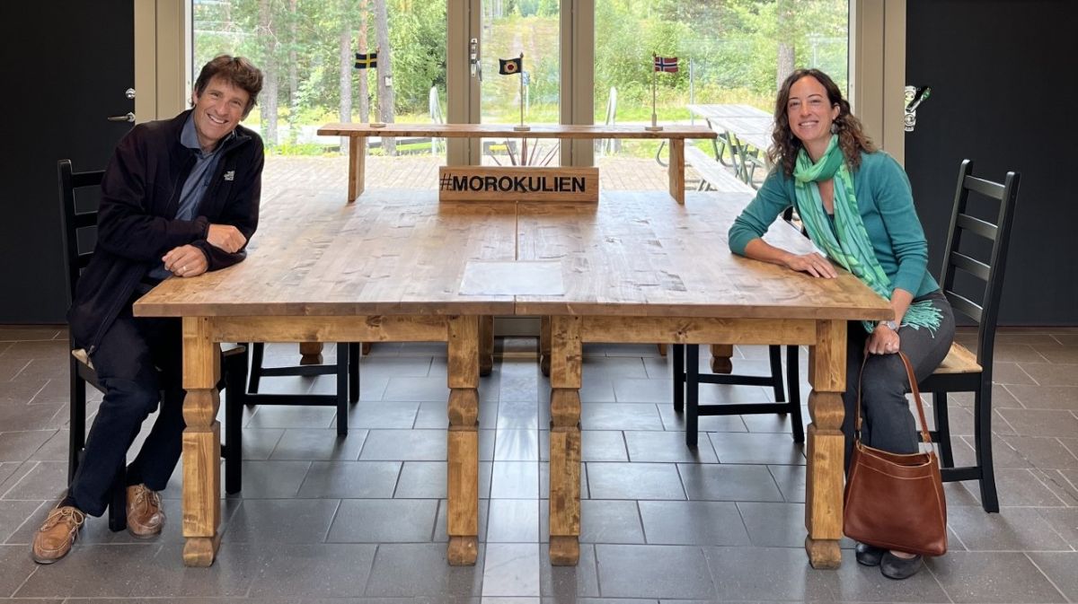 A middle-aged light-skinned man and middle-aged light-skinned woman, both brown-haired, sit across from each other at a wooden table.