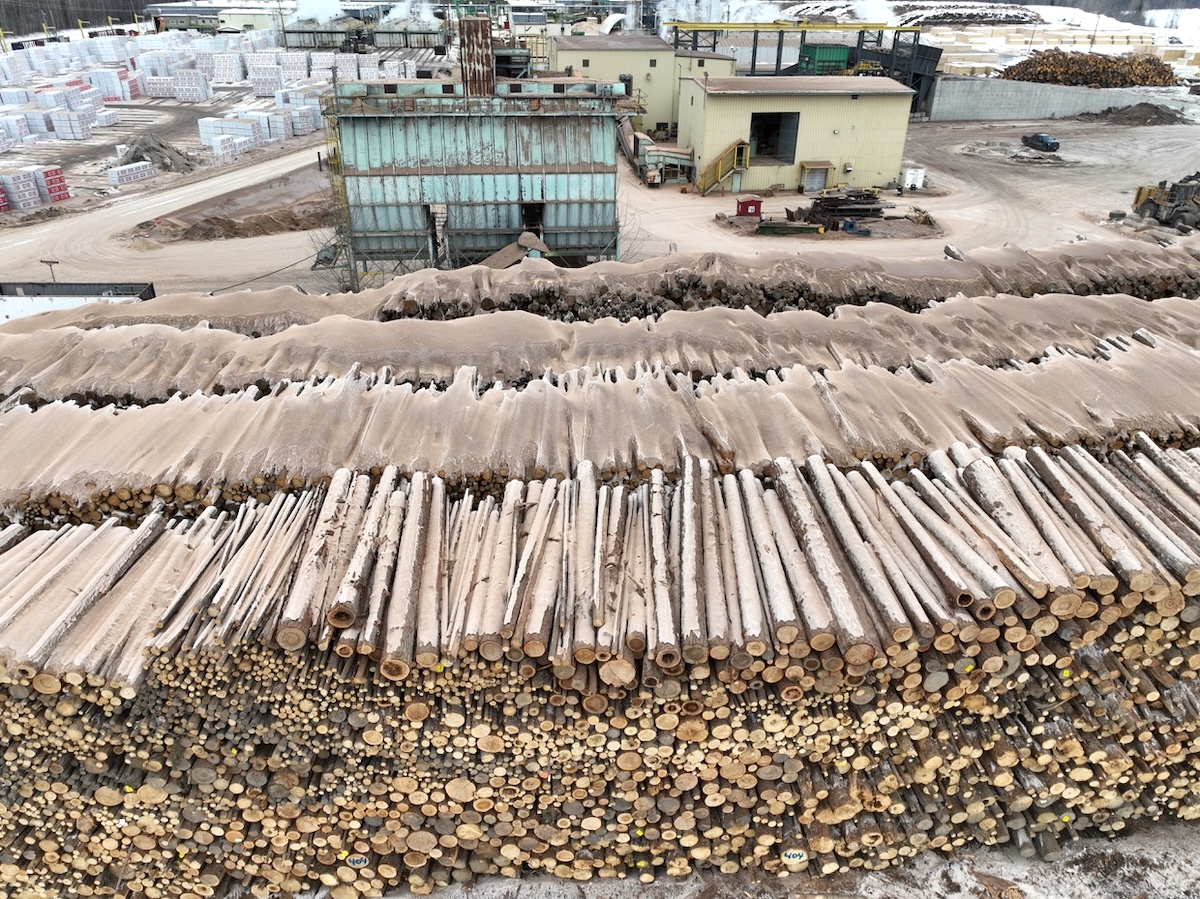 An aerial photo shows piles of logs dusted in snow.