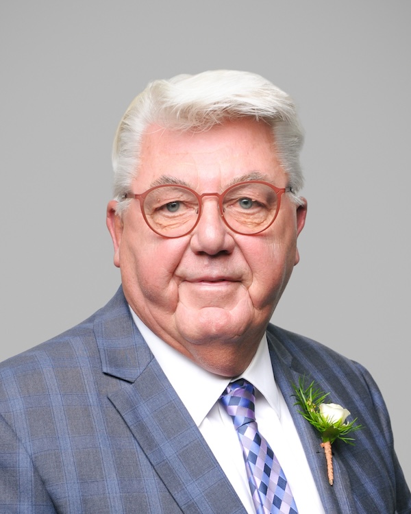 A portrait-style photo of a light skin-toned person with short white hair, round-frame glasses and wearing a blue and black checkered jacket.

