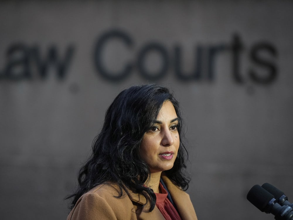 Attorney General Niki Sharma, a woman with medium skin tone and straight dark hair, stands in front of the Law Courts in Vancouver.