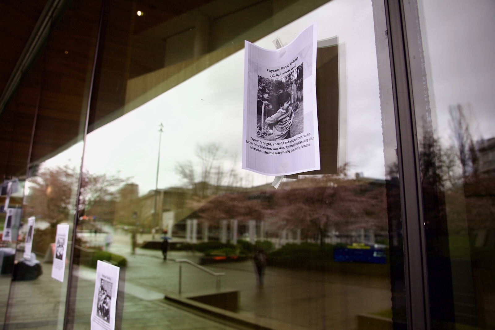 Posters of letter-sized paper bearing a photo of a young child are taped to a glass window.