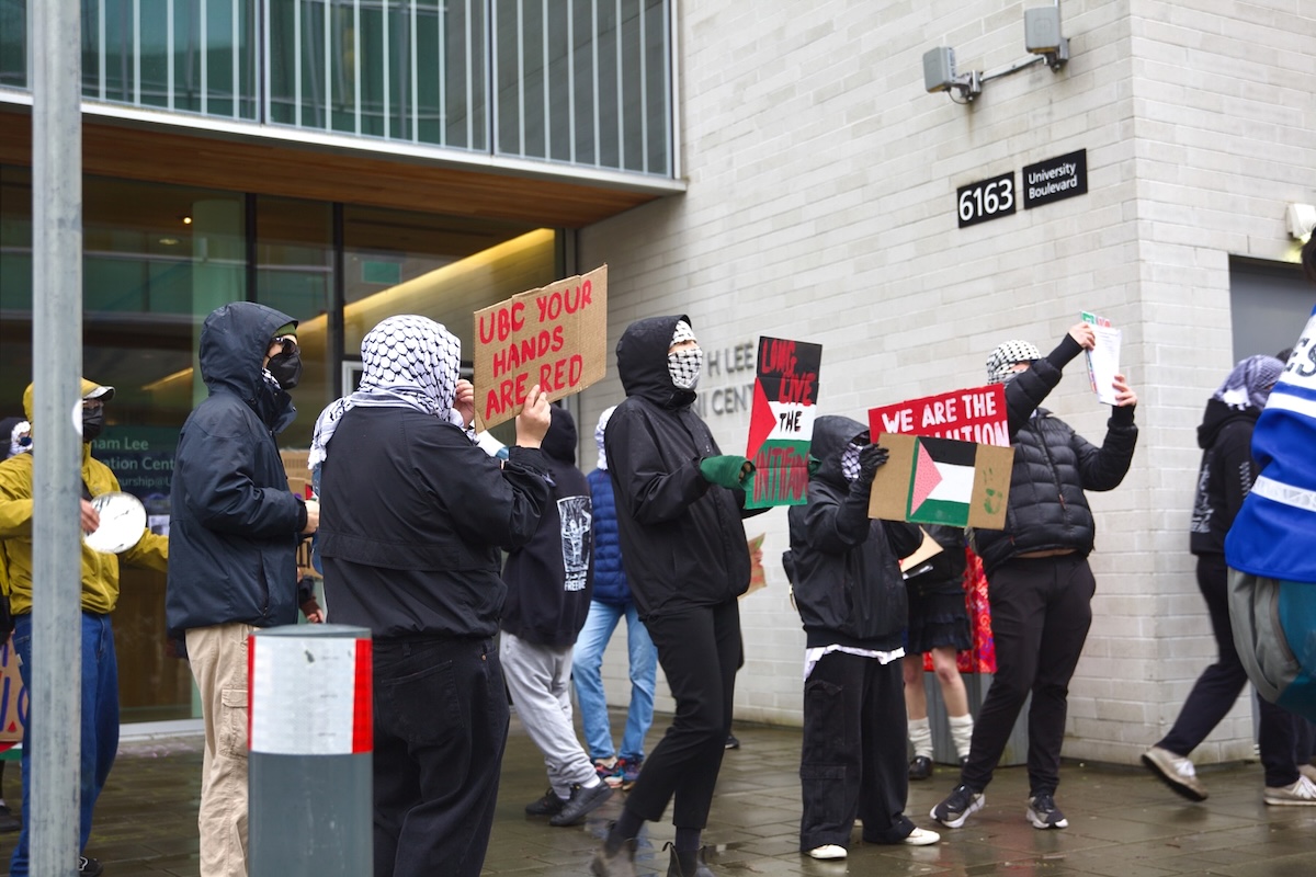Students wearing kaffiyehs and face coverings hold cardboard protest signs.