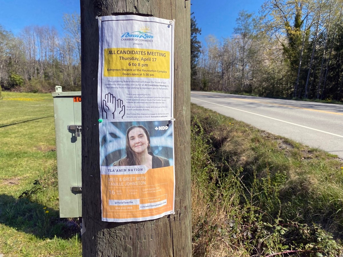 Two posters are stapled to a wooden pole at the south end of tišosəm. One advertises the all-candidates meeting in Powell River. The other advertises a meet-and-greet with NDP candidate Tanille Johnston in tišosəm.