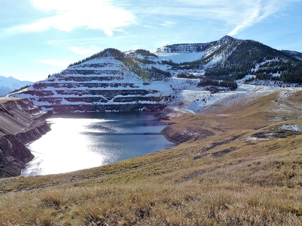 A photo shows a mountain with terraced remains of former coal mining, with a tailings pond in the foreground.