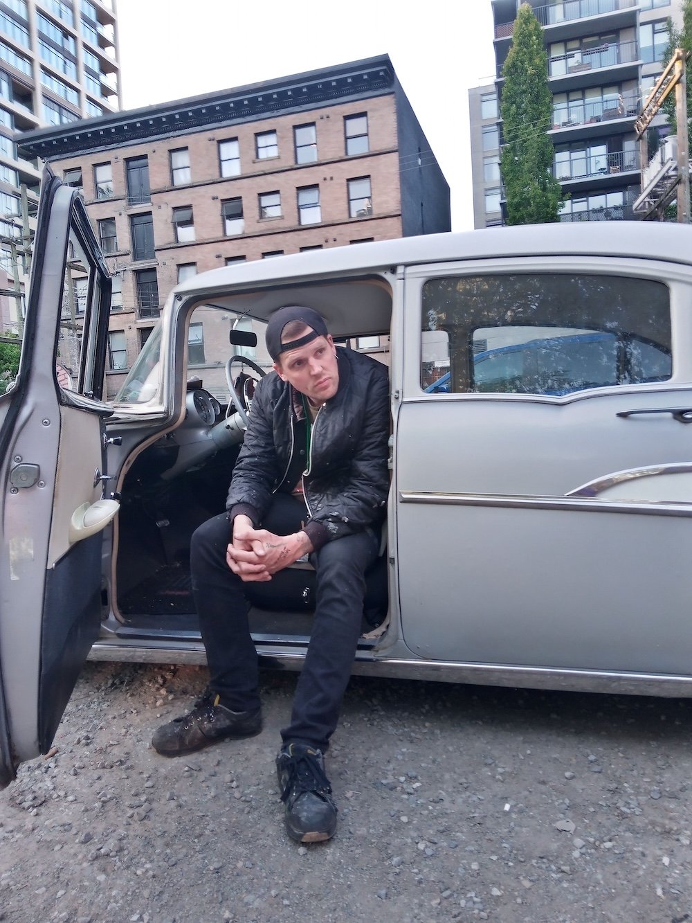 Trey Helten sits in a vintage car, with the door open.
