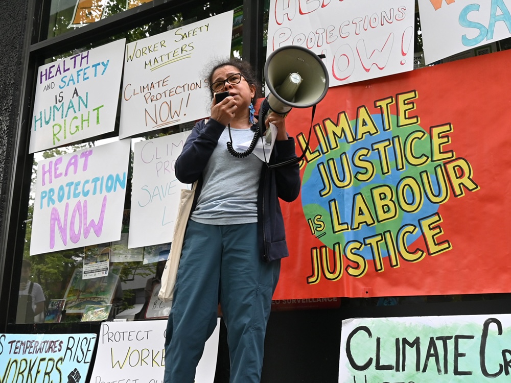 Ingrid Mendez, a woman with medium-light skin tone, glasses and dark hair, gives a speech outside David Eby’s MLA office.