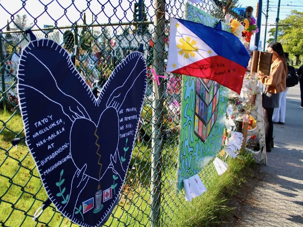 A chain-link fence outside a grassy area holds signs, flags and notes.