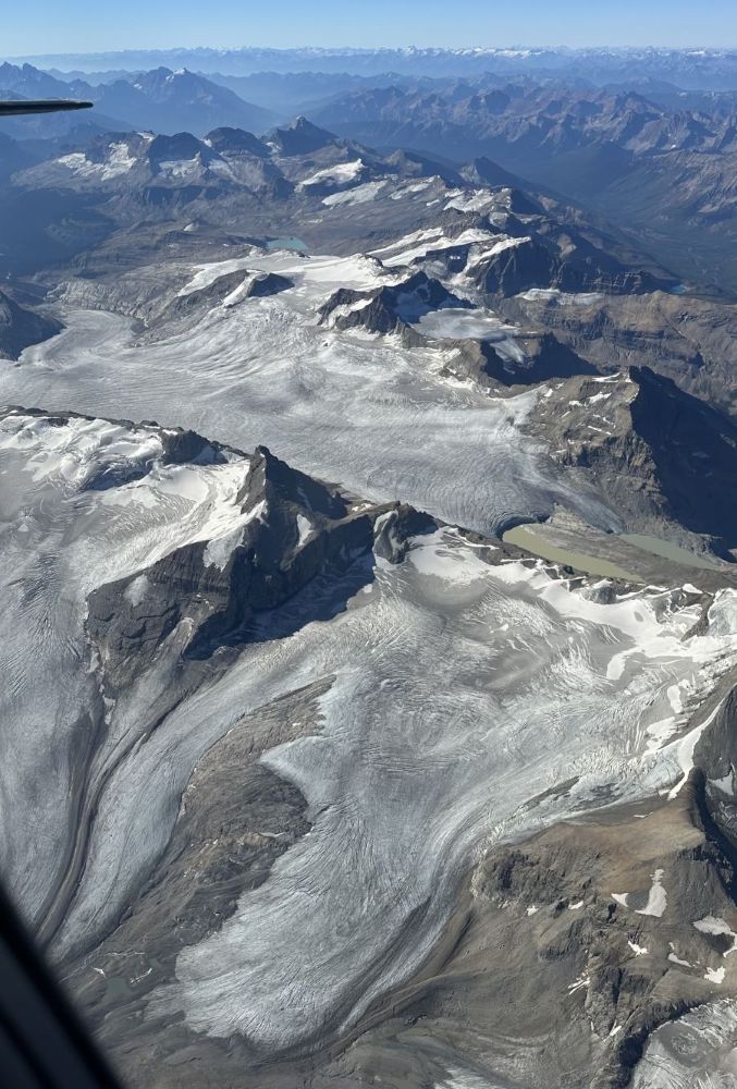An aerial photograph shows mountains and glaciers that are stained grey.