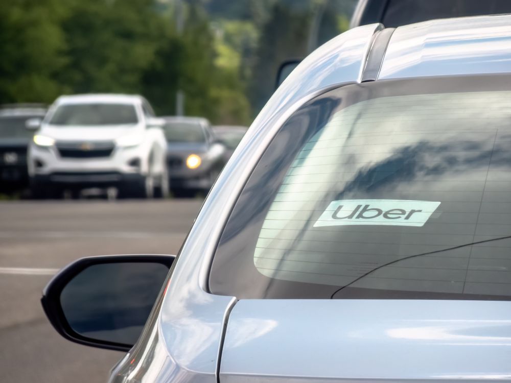 A grey car sits in a parking lot with a sign in the window saying Uber.