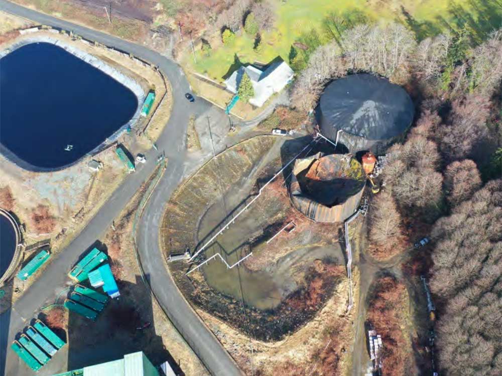 An aerial photo shows a large cylindral tank that has collapsed. The ground around it looks wet and sludgy. It is beside an intact tank.