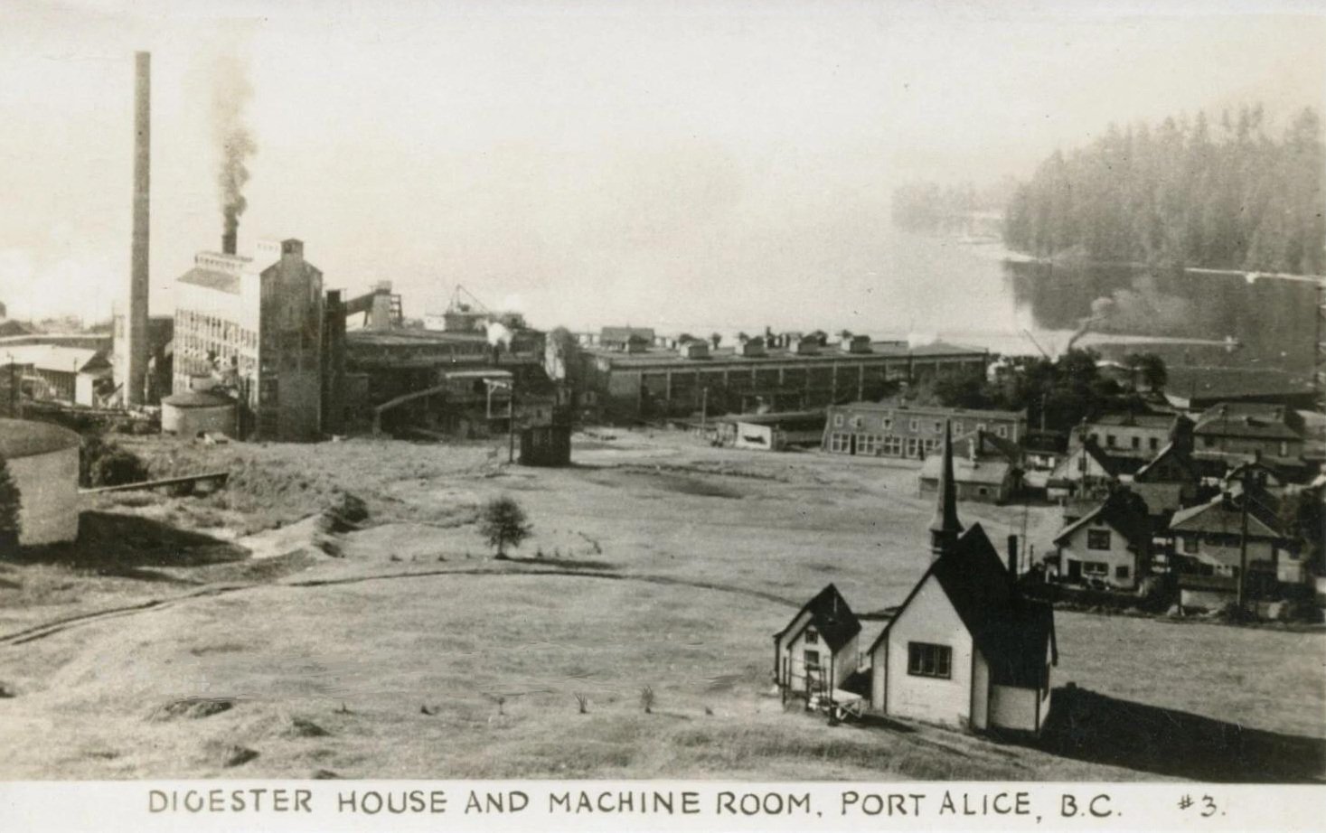 A black and white photo shows houses in the foreground, and the mill in the background by the inlet.