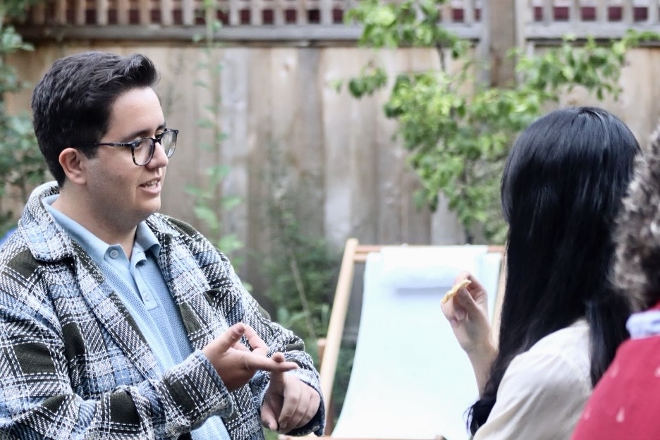 A young man with brown hair and glasses gestures as he speaks to a potential supporter at a political event.