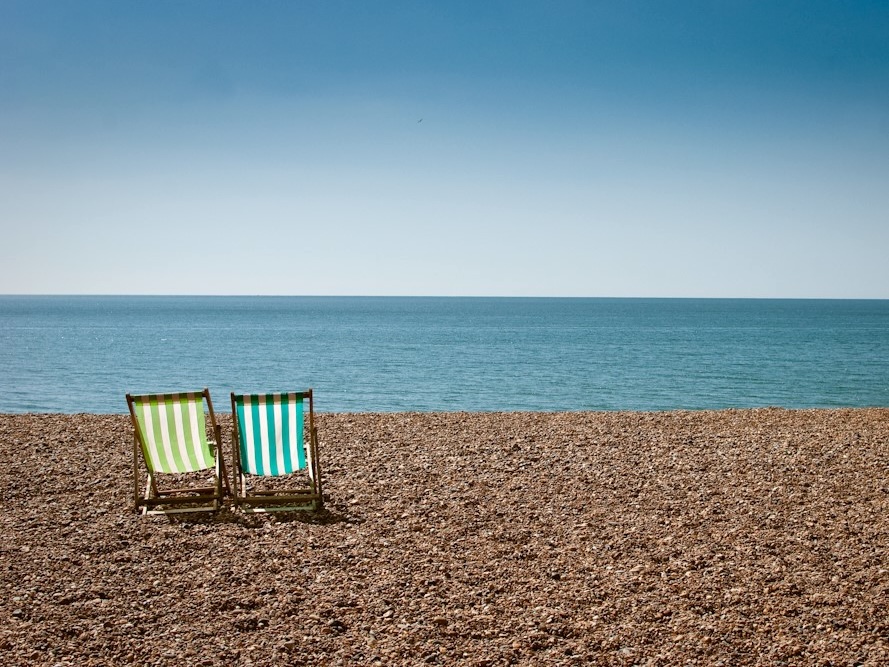 Two striped beach chairs with no one sitting in them on a beach with the ocean in the distance.