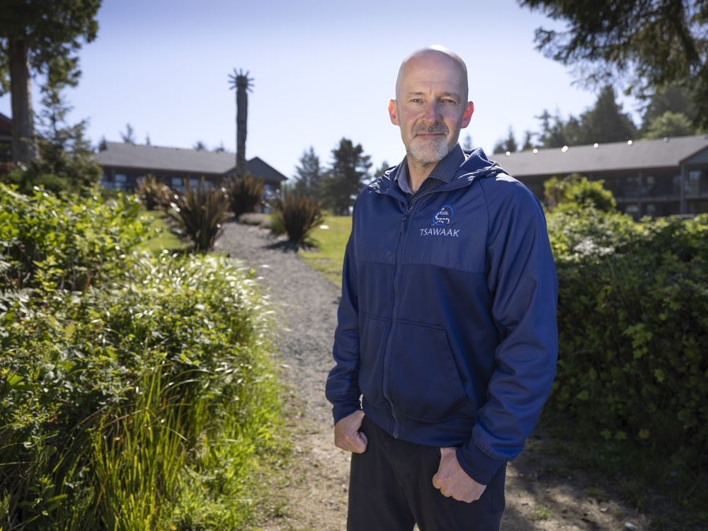 Jared Beaton, a bald man with a grey beard and light skin tone wearing a dark blue windbreaker, stands on the grounds of a coastal resort.
