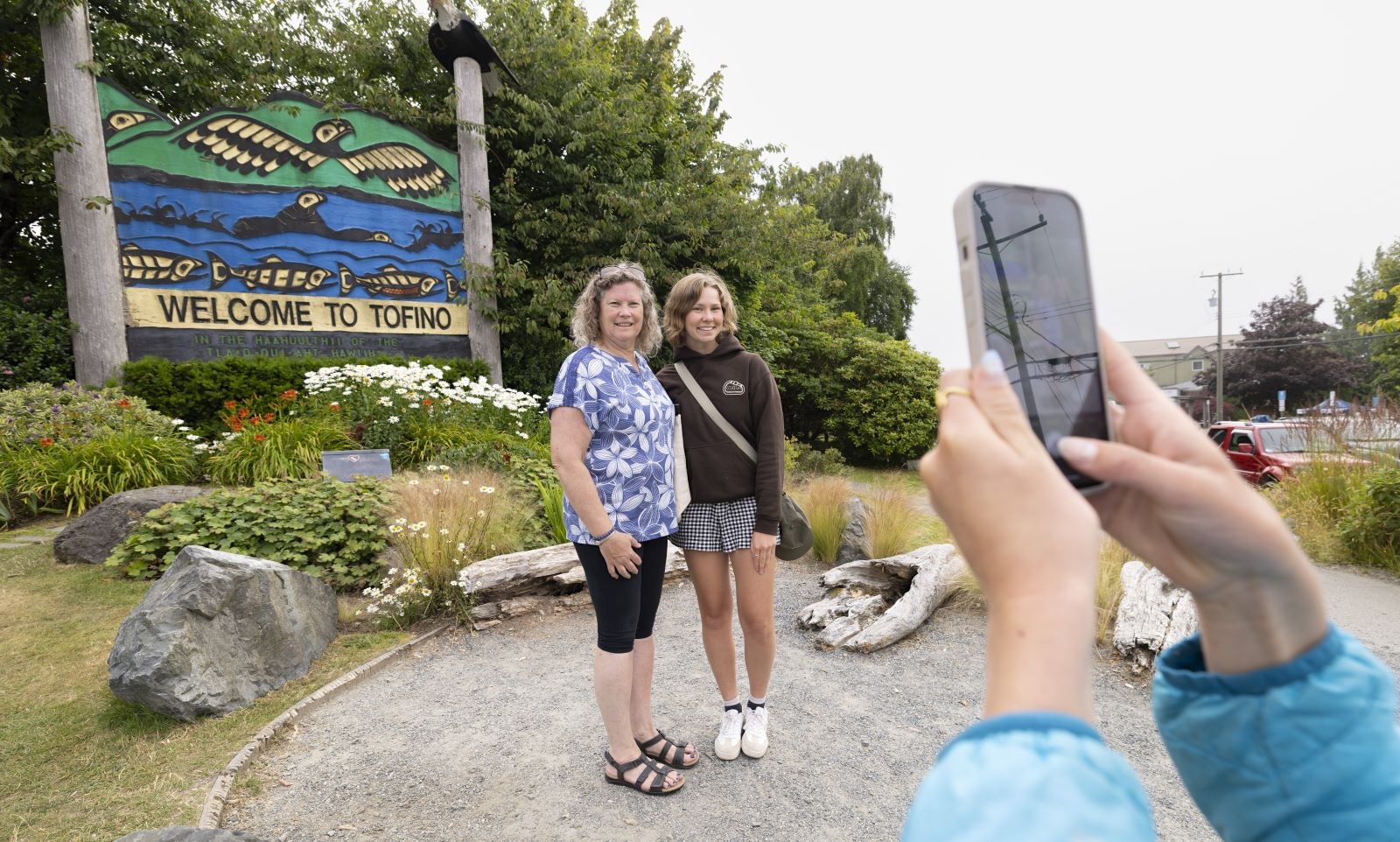 Two women pose for a photo in front of a &lsquo;Welcome to Tofino&rsquo; sign.