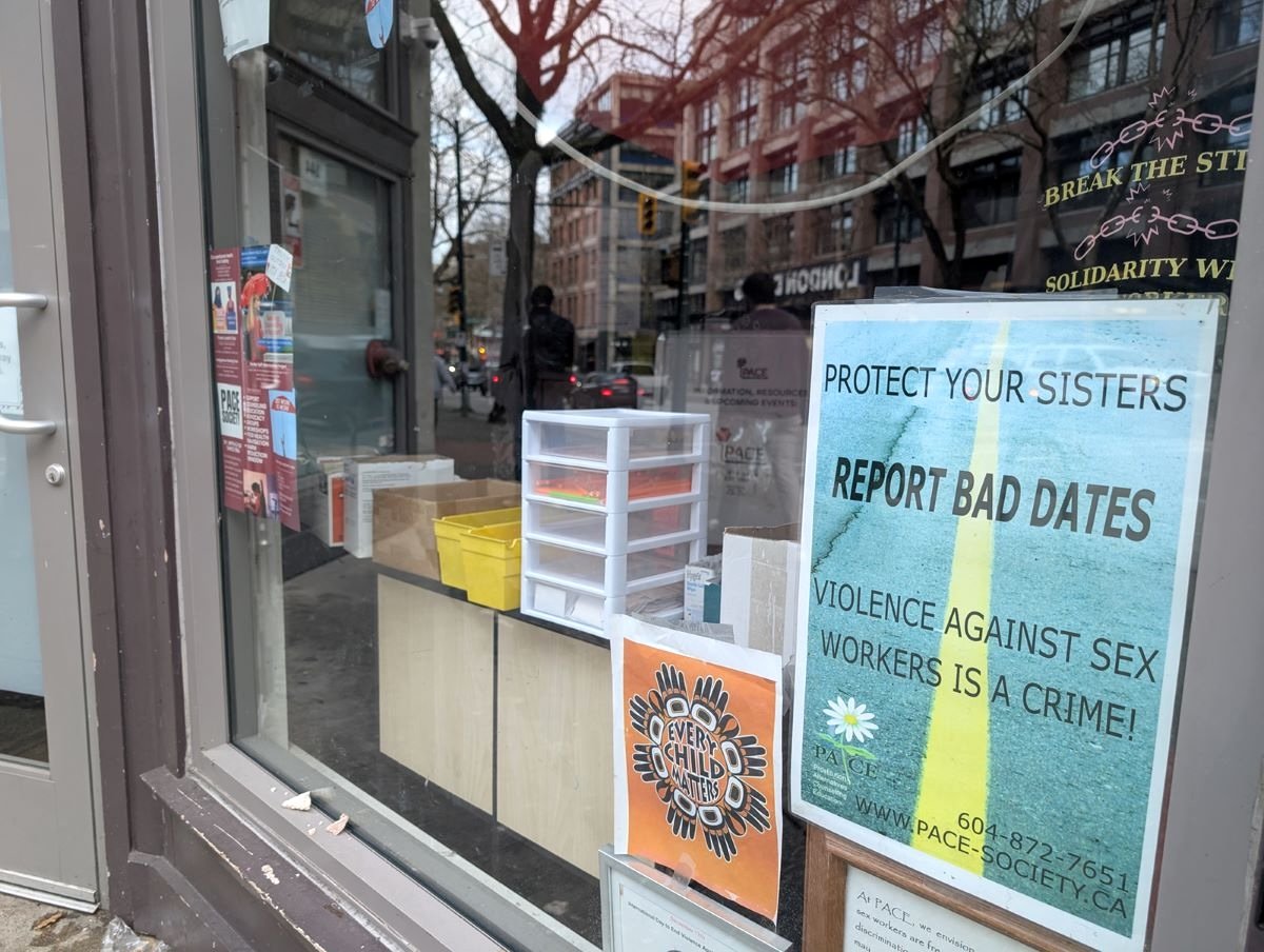 A storefront in the Downtown Eastside. In the window is an ‘Every Child Matters’ poster and a ‘Protect Your Sisters: Report Bad Dates’ poster.