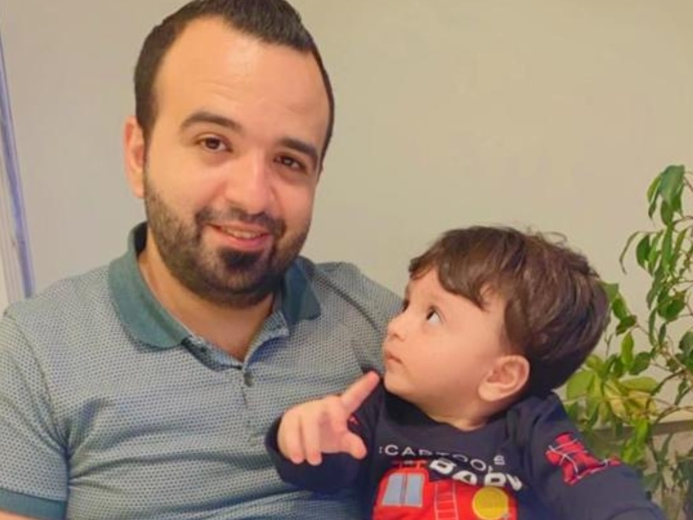 A man with medium-light skin tone and short dark hair and beard holds a young boy with similar colouring.