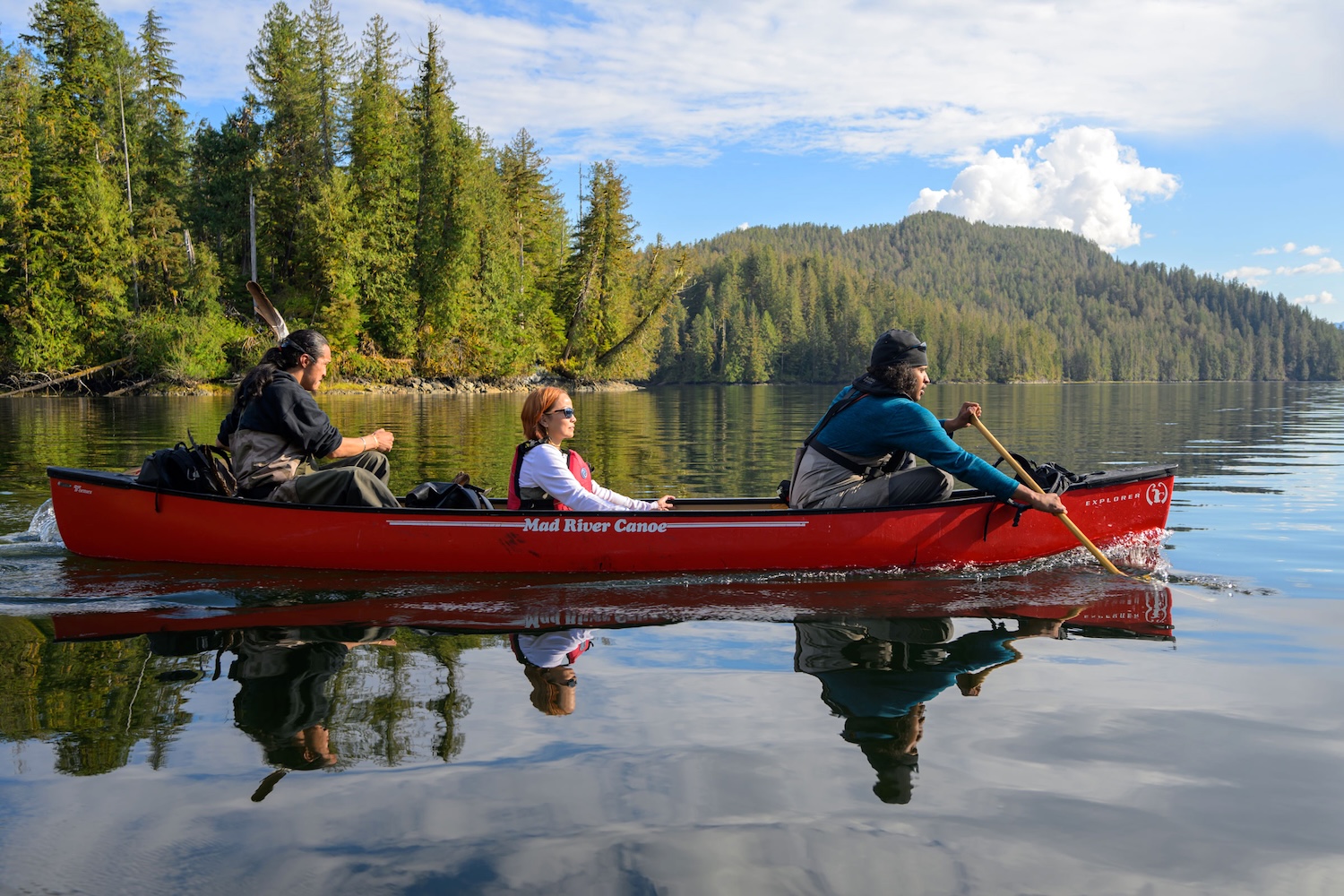 Three people paddle in a canoe on calm water.
