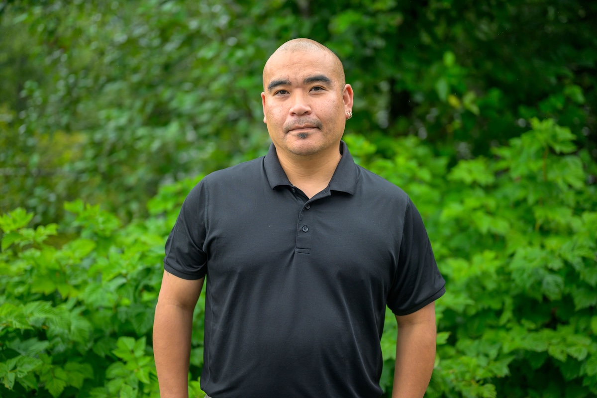 Doug Neasloss, a man with very close-cropped hair and medium-light skin tone, looks at the camera. He is wearing a black, short-sleeved polo shirt.