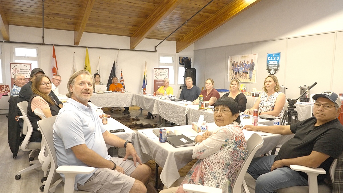 About 14 people sit around four tables in a square, in a meeting room.
