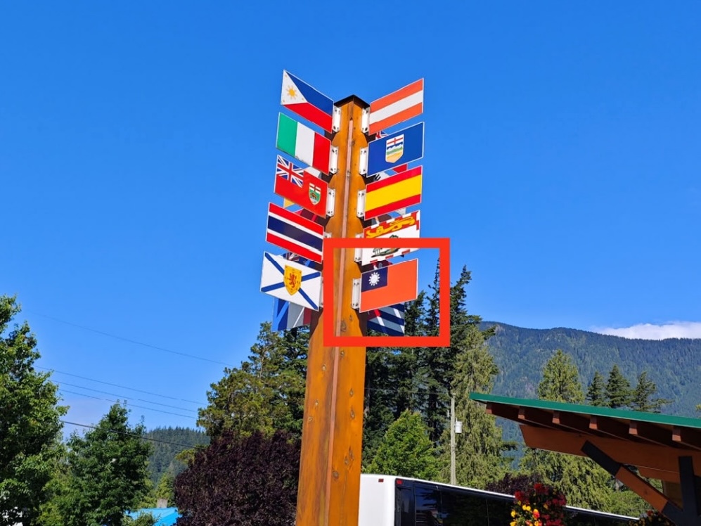 A number of flags are mounted on a pole, including one, framed in a red box, that shows a white rounded star set against a blue field in the corner of a flag that is otherwise red.