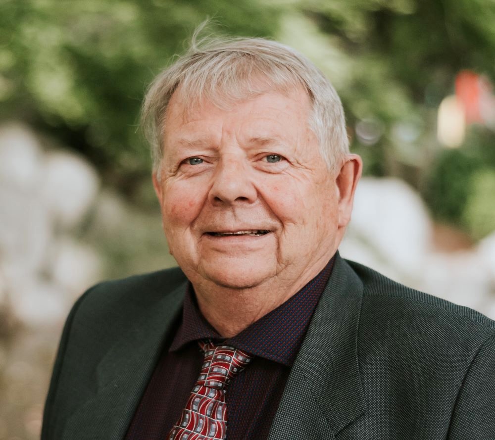 A smiling grey-haired white man of about 60 wears a suit and tie.