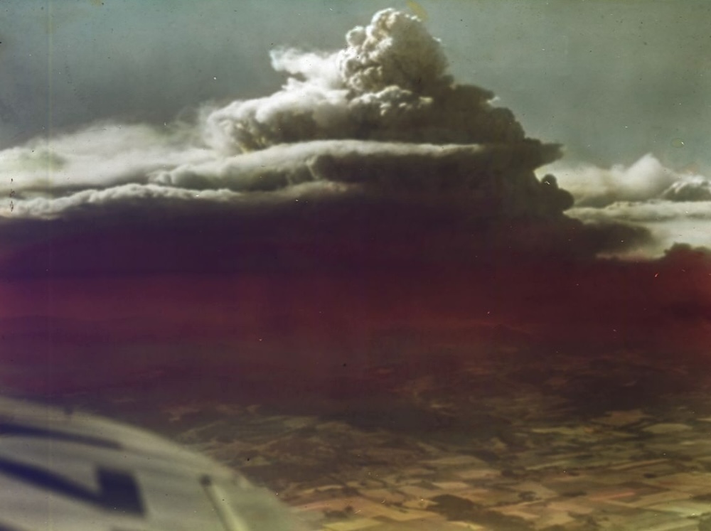A colourized photo, shot from an airplane, of a massive smoke plume.