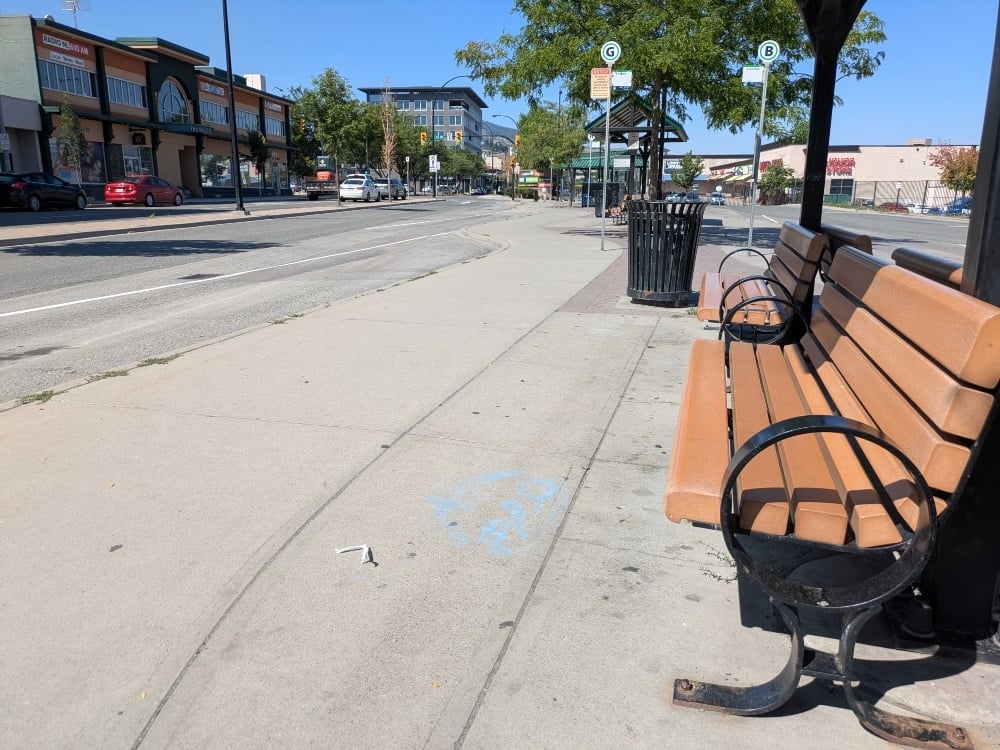 A bench sits empty at a downtown bus exchange on a sunny day.