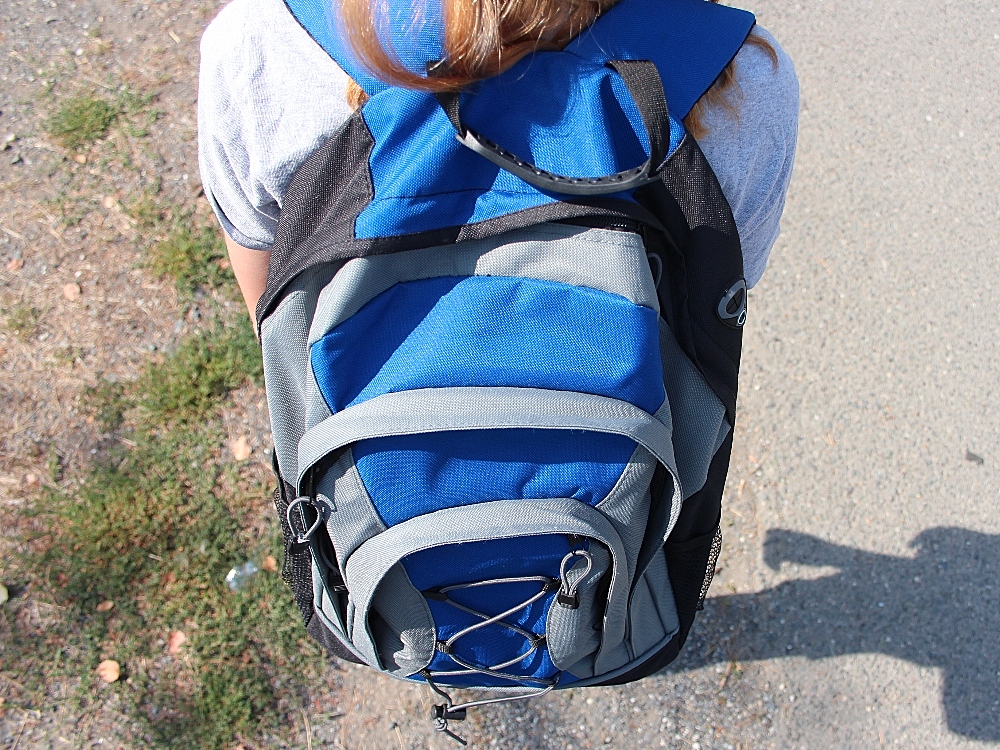 A student wearing a bright blue backpack stands with her back to the camera.