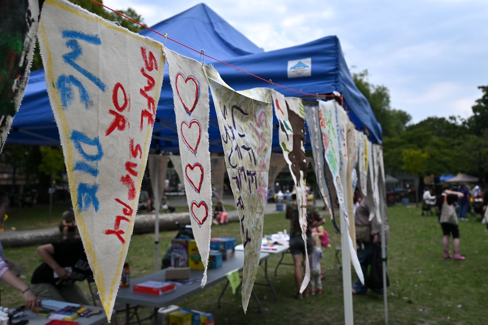 Hand-painted triangular pennants hang from a stretched line, the closest one with the words &lsquo;Safe Supply or We Die.&rsquo;