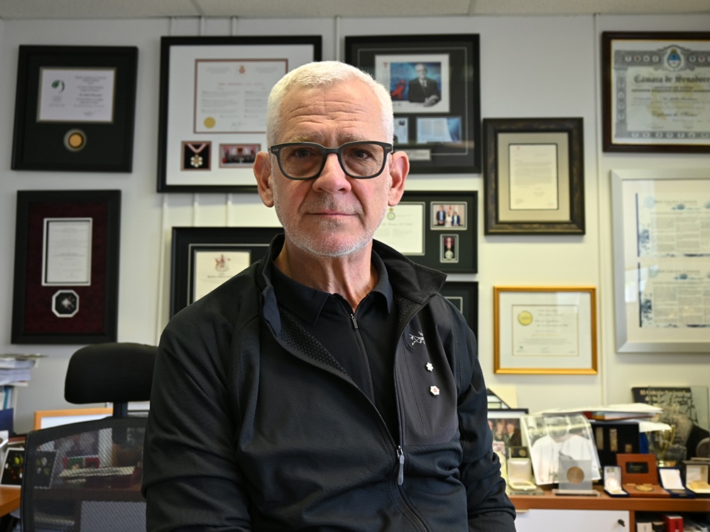 A man with light skin tone and close-cropped grey hair wears black-framed glasses.