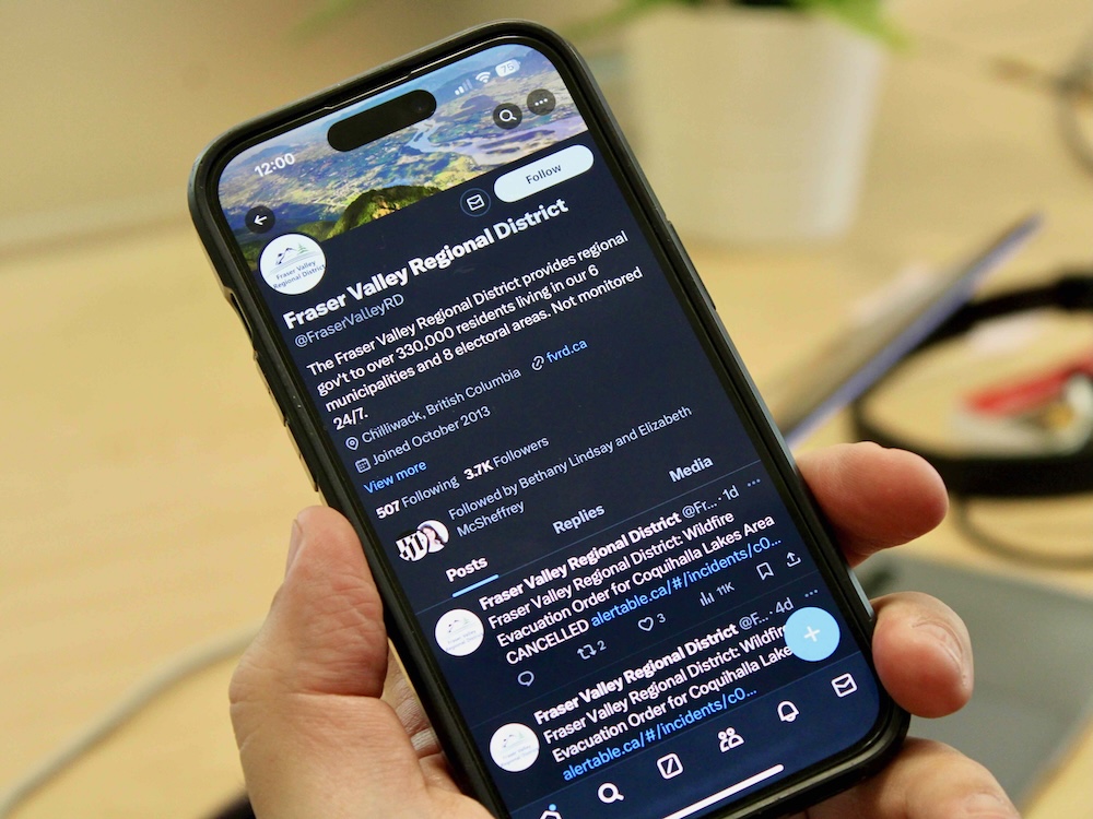 A hand holds a smartphone open to the X account of the Fraser Valley Regional District.