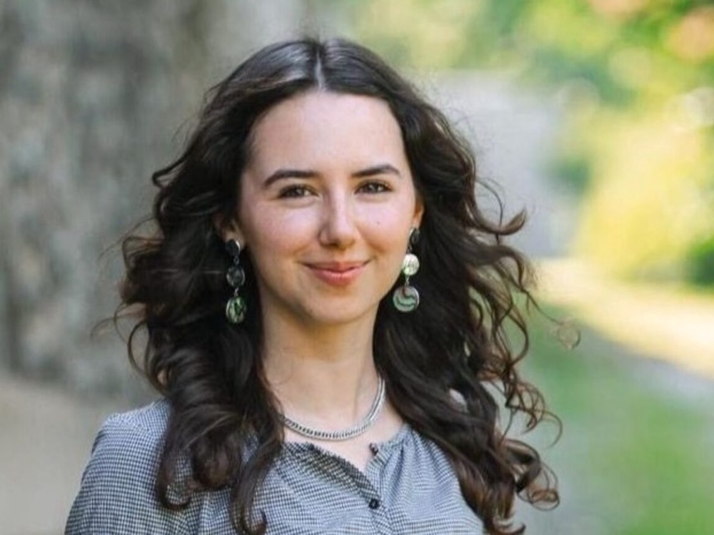 A 24-year-old light-skinned woman with long dark hair smiles.