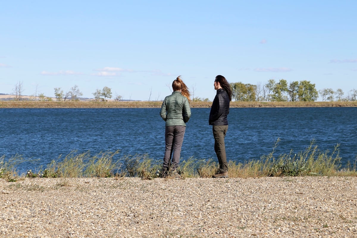 Two women stand with their backs to the camera. In front of them is a water reservoir.