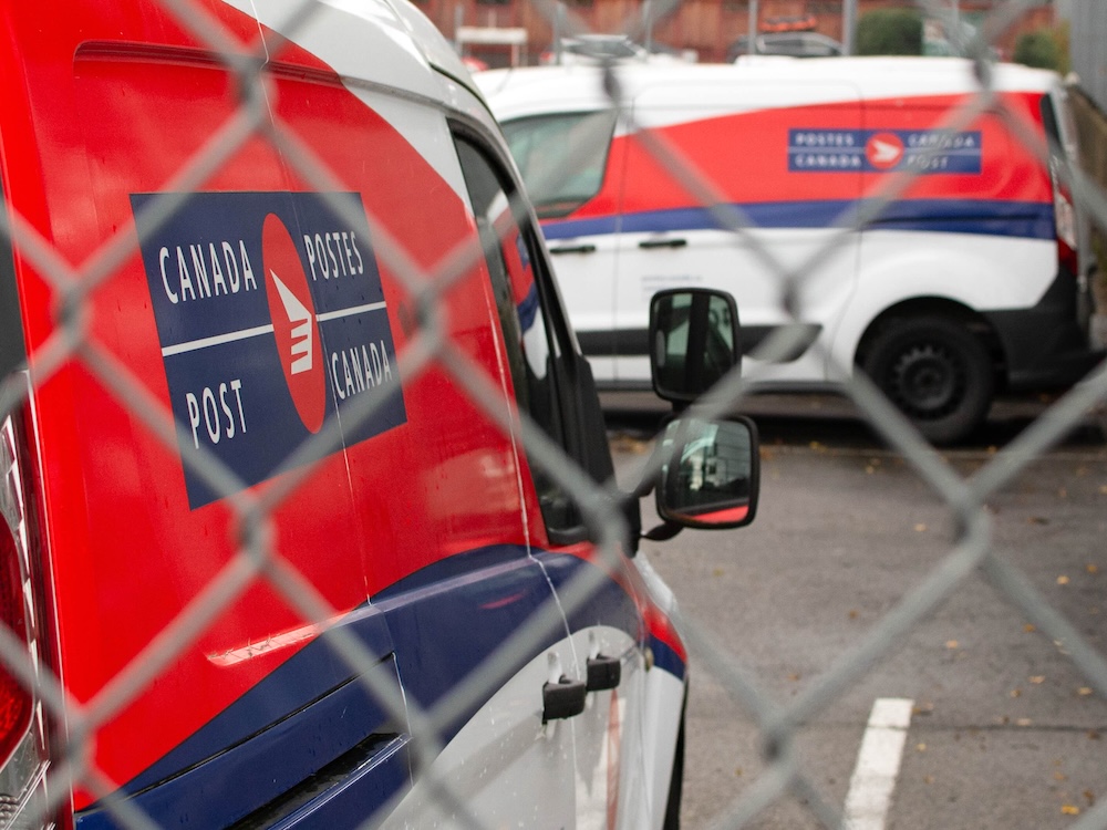 Trucks with the red Canada Post logo are behind a chain-link fence.