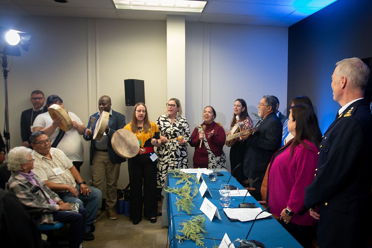 People with drums line the wall in a crowded room as others look on.
