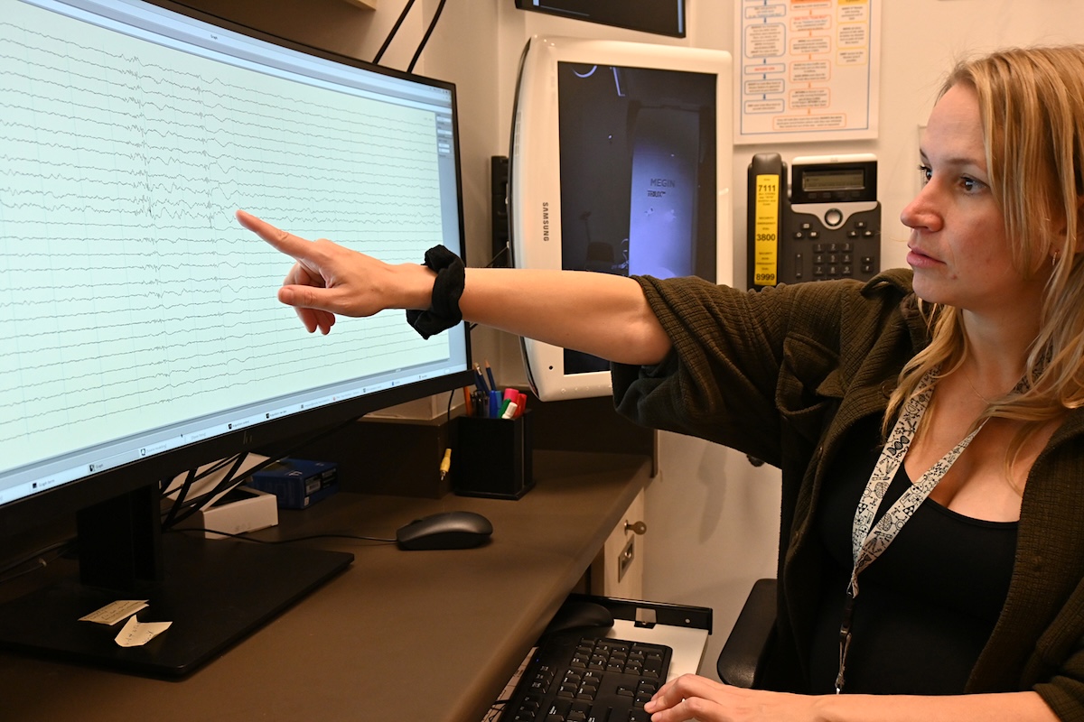 A woman with light skin tone and shoulder-length blond hair shows a display with a number of squiggly lines.