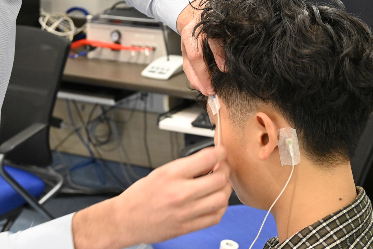 A person reaches over and tapes a movement-tracking electrode on another person&rsquo;s head.
