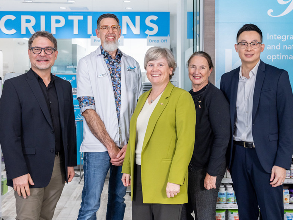 Three men and two women pose for a photo in a pharmacy. 