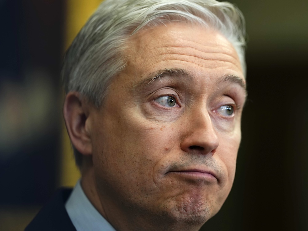 A middle-aged man with white and grry hair and light skin makes a bemused expression.