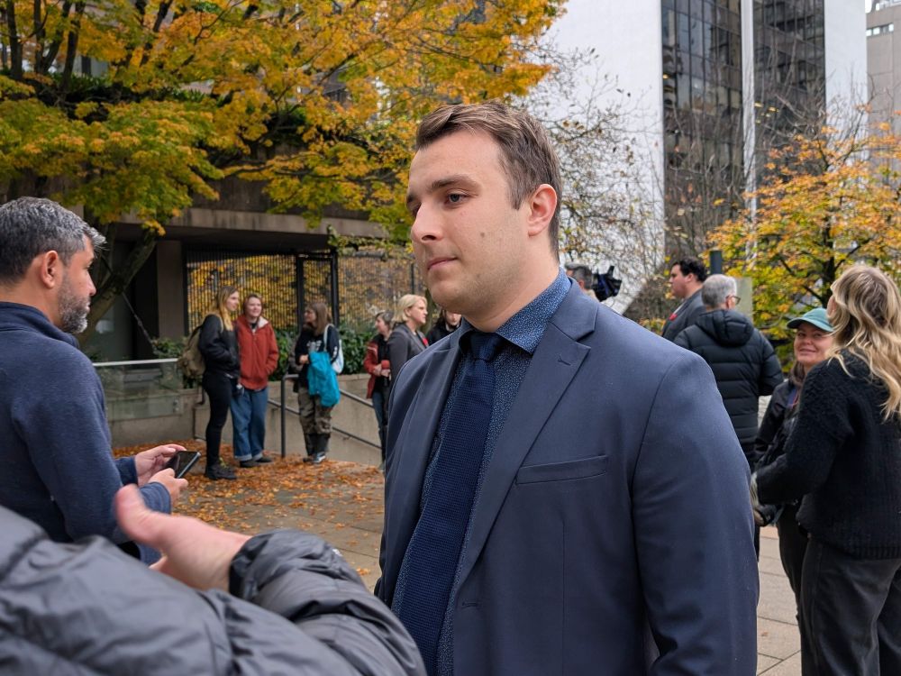 A 30-ish light-skinned man in a blue suit stands outside.
