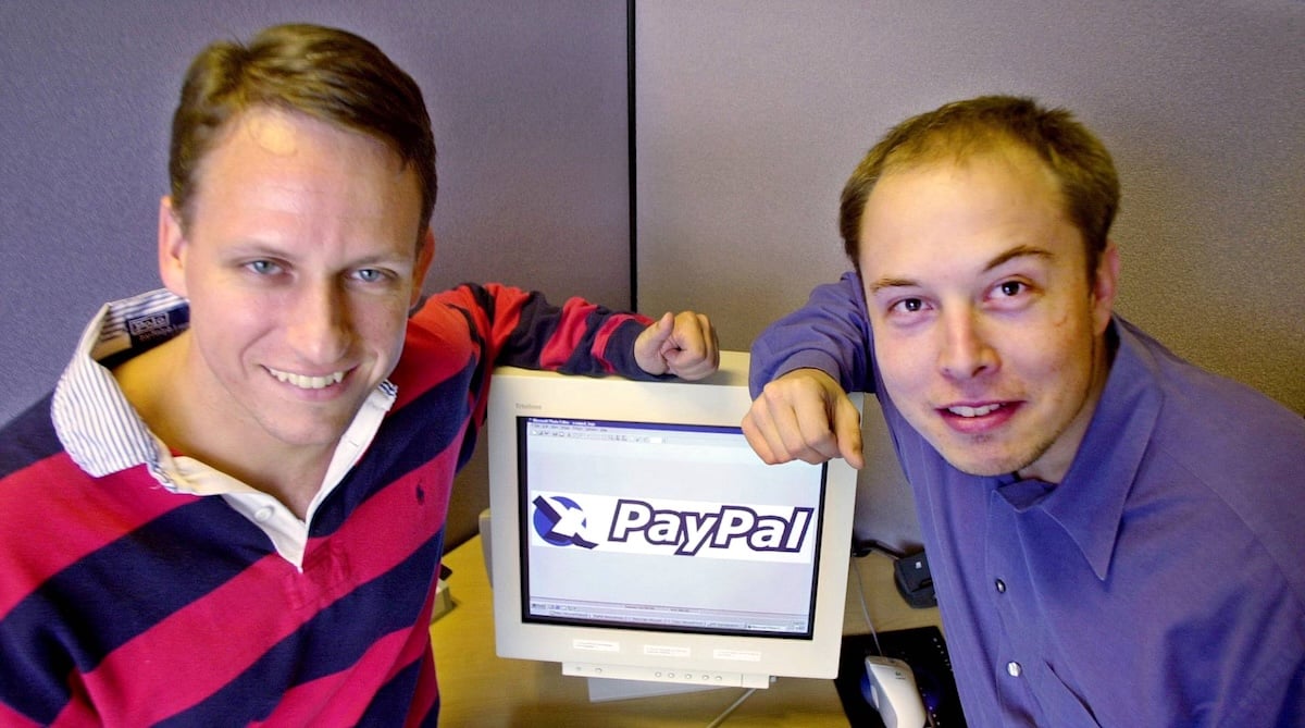 Two young men with light skin and brown hair on either side of an old-model computer screen displaying a ‘PayPal’ logo.