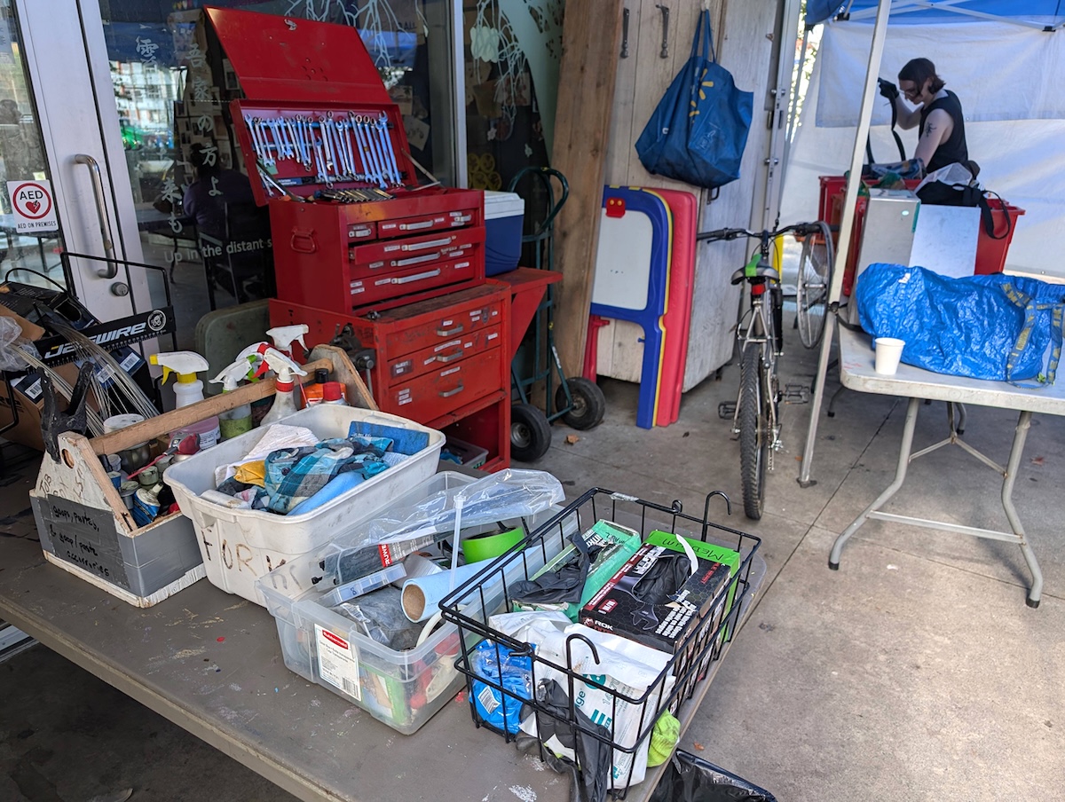 Bins of gloves, cables, housing and other items appear in the foreground. A large red tool chest appears in the background.