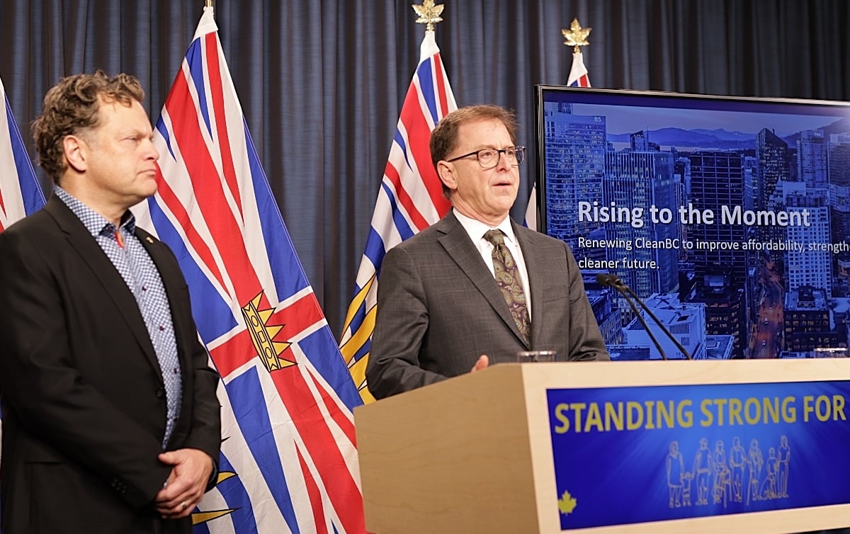 Adrian Dix is fair skinned and is wearing a suit and tie. Jeremy Valeriote, also with fair skin, has hands clasped in front of him and is looking on, not appearing too pleased.